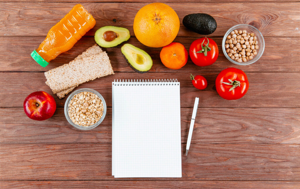 Blanche de bois avec plusieurs aliments comme avocat, orange, pomme... et avec un carnet et un stylé afin de mettre en avant la planification pour manger plus dans le but de maigrir 